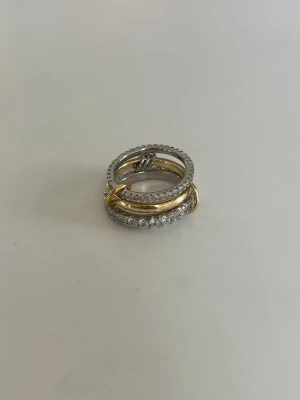 ring  - Säljer en unik stapelring i både silver- och guldfärg. Ringen består av flera ringar i olika utföranden, varav en är dekorerad med gnistrande stenar. Perfekt för dig som gillar att mixa metaller och vill ha något som sticker ut.
