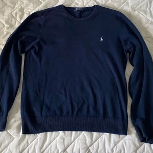 Mörkblå tröja från Polo Ralph Lauren - Mörkblå långärmad tröja från Polo Ralph Lauren med rund halsringning och broderad logga på bröstet. Perfekt för en stilren och klassisk look.