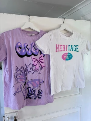2st t-shirt med tryck för flickor  - 2st T-shirt med tryck för flickor. En lila t-shirt med coolt tryck i graffiti-stil, stor fjäril, rosett och texten 'Love' på framsidan från H&M. T-shirten har korta ärmar och avslappnad passform.  En vit med tryck som det står ”Heritage” från Cubus.