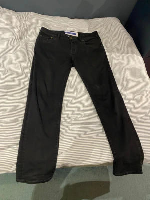 Jacob Cohen Scott strl 31 - Snygga svarta jeans från Jacob Cohen med klassisk femficksmodell och raka ben. Jeansen har diskreta sömmar och metallknappar. Perfekta för dig som gillar stilrena och tidlösa plagg. Materialet känns mjukt och följsamt. Modellen 182 cm. Hör av er vid frågor och funderingar!