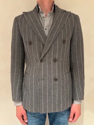 Dubbelknäppt Randig Suitsupply Kavaj - En grå bläser från Suitsupply med vita ränder. I ett mycket fint 100% ull tyg från Italien. Storlek 48 och slim fit, sitter helt okej på mig som är 186 och 77kg. Inga märken eller defekter och nyss kemtvättad. 