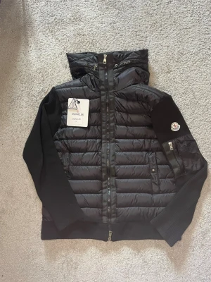 Svart pufferjacka - Snygg svart pufferjacka från Moncler med quiltad front och huva. Jackan har stickade ärmar och muddar, dragkedja framtill samt fickor med dragkedja. Denna är i storlek M/S vid frågor är det bara att skriva //MVH pris 1099: