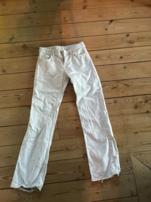 Vita raka jeans med slitningar - Säljer ett par vita jeans med rak passform och slitna detaljer vid knä och benslut. Klassisk femficksmodell och normal midja. Perfekta för en avslappnad och trendig look.