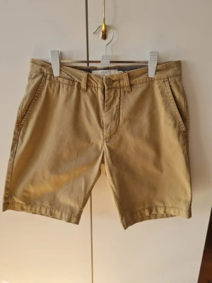 Beige chinosshorts från H&M strl W29 - Snygga beige chinosshorts från H&M med klassisk design. De har en knapp och dragkedja framtill samt två sidofickor och två bakfickor med knappar. Storlek EUR 29. Kan hämtas i Vallentuna.