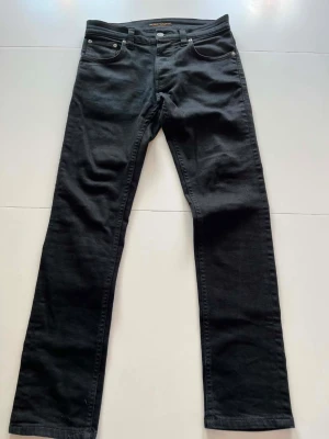 Svarta jeans från Nudie Jeans - Snygga svarta jeans från Nudie Jeans med klassisk femficksdesign och raka ben. Jeansen är av modell grim tim och är storlek 30/30. 