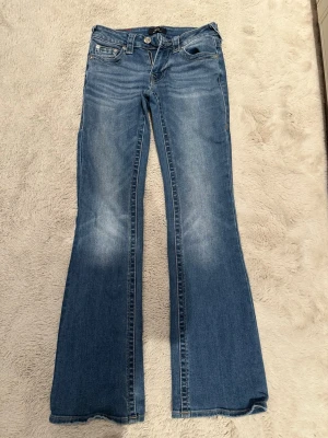 Blå bootcut jeans från True Religion  - Snygga blå bootcut jeans från True Religion med klassisk femficksdesign och lätt slitna detaljer framtill. Jeansen har normalhög midja och är tillverkade i mjuk denim med stretch för extra komfort. Perfekta för en avslappnad och trendig look. Är i jättebra skick