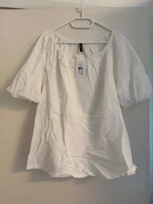Vit blus med puffärm från kappahl - Luftig vit blus från H&M med diskret randig struktur. Blusen har korta puffärmar med resår vid ärmslut och är tillverkad i ett lätt tyg som ger en avslappnad känsla.