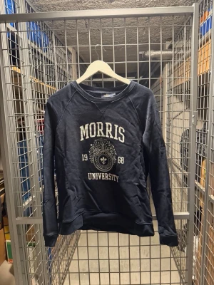 Morris University sweatshirt marinblå - Marinblå sweatshirt från Morris med tryck 'Morris University 1968' och emblem framtill. Tröjan har rund halsringning, långa ärmar och ribbade muddar vid ärmslut och nederkant. Perfekt för en avslappnad och sportig stil.