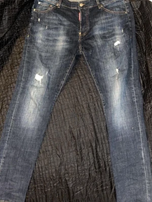 Mörkblå slitna jeans med raka ben storlek 54 - Säljer ett par mörkblå jeans med slitningar och hål på låren. Jeansen har raka ben, klassisk femficksmodell och tydliga tvättade detaljer. Perfekta för en avslappnad och trendig look.