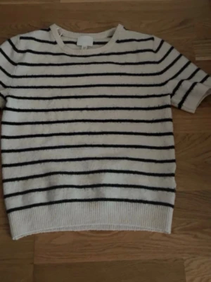 Randig kortärmad tröja från H&M - Snygg kortärmad tröja från H&M i krämvitt med svarta horisontella ränder. Tröjan har rund halsringning och ribbade kanter. Perfekt för en avslappnad och trendig look.