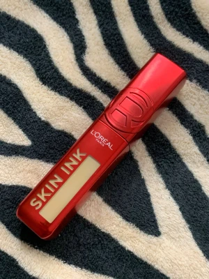 L'Oréal Skin Ink foundation  - Läckert foundation från L'Oréal Paris i serien Skin Ink. Höljet är metallicrött med tydlig logga och modern design. Läppstiftet har en rektangulär form och är tillverkat i plast. Perfekt för dig som vill ha en snygg och trendig look.