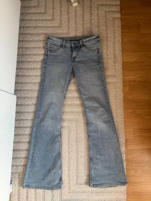 Ljusblå bootcut jeans - Säljer ett par ljusblå bootcut jeans med klassisk femficksdesign och normal passform. Jeansen har en snygg tvätt och är perfekta för dig som gillar en retroinspirerad look. Stängs med knapp och dragkedja framtill.