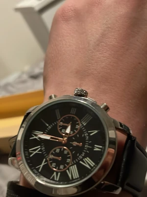 Svart klocka med romerska siffror - Stilren klocka från Michael Kors med svart urtavla, romerska siffror och tre mindre urtavlor. Boetten är i silverfärgad metall och armbandet är i svart skinn. Perfekt accessoar för en snygg och klassisk look.