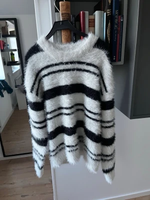 Fluffig randig stickad tröja - Säljer en supermjuk och fluffig stickad tröja med svarta och vita horisontella ränder. Tröjan har lång ärm, rund halsringning och en oversized passform. Perfekt för dig som gillar en cozy och trendig look.