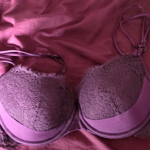 Lila spets-bh från Hunkemöller - Snygg lila bh från Hunkemöller med vadderade kupor och vacker spetsdetalj över hela framsidan. Bh:n har dubbla axelband på ena sidan för en trendig look och justerbara band för bästa passform. Perfekt för dig som vill ha något både bekvämt och stilrent.