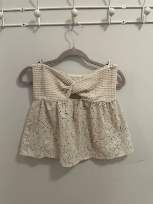 Beige tub topp - Supersöt beige tub topp med broderade blommor och twistad detalj framtill. Toppen är axelbandslös och har en luftig passform, perfekt för varma dagar. Materialet känns som bomull och ger en romantisk vibe. Storleken är XS men passar även S