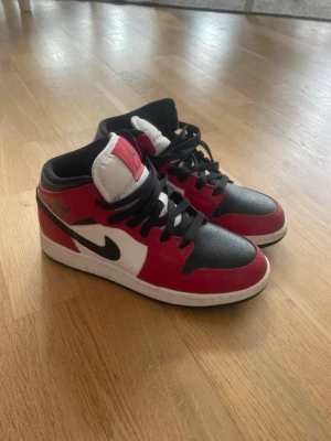 Nike Air Jordan 1 Mid röd/svart/vit - Säljer ett par Nike Air Jordan 1 Mid sneakers i klassisk röd, svart och vit färgkombination. Skorna har svart swoosh, svarta skosnören och detaljer i läder. Ikonisk Jumpman-logga på plösen och Air Jordan-vinge på sidan. Perfekta för dig som gillar streetwear.  Använda endas 1 gång så är i mycket bra skick.