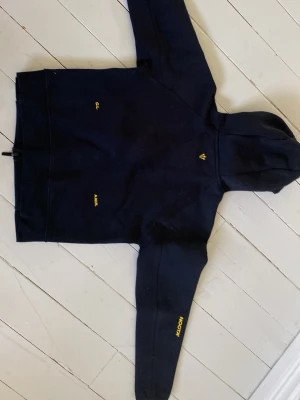 Svart Nike hoodie med gul logga - Snygg svart hoodie från Nike med dragkedja och huva. Framtill finns två fickor med svarta dragkedjor och en gul Nike-logga på bröstet. På baksidan syns små gula broderade detaljer. Perfekt för en sportig och avslappnad stil.