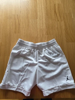 Nike Jordan basket vita shorts, NBA , Dam storlek S - Säljer ett par vita sportiga shorts från Jordan med den klassiska Jumpman-loggan broderad i svart på benet. Shortsens material är lätt och andas, perfekt för träning eller basket. De har elastisk midja för skön passform.