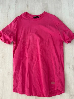 Rosa t-shirt från Bershka - En enkel och stilren rosa t-shirt från Bershka i mjuk bomull. T-shirten har rund halsringning och korta ärmar. Perfekt basplagg att matcha med jeans eller kjol. Liten Bershka-logga nertill på framsidan.