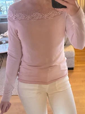 Ljusrosa topp med spetsdetalj - Supersöt ljusrosa topp med lång ärm och vacker spets upptill vid halsringningen. Toppen har en feminin och stilren look, perfekt att styla med jeans eller kjol. Mjuk och skön känsla mot huden.