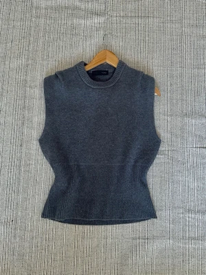 Mörkgrå stickad väst med hög hals - Snygg mörkgrå stickad väst med hög hals och ribbad midja. Perfekt att styla över en skjorta eller t-shirt för en trendig lager-på-lager-look. Västen har en figurnära passform och är supermjuk och bekväm. Från Zara!
