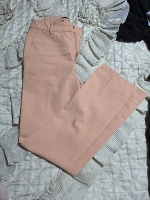 Beige kostymbyxor från Bik Bok - Snygga beige kostymbyxor från Bik Bok i storlek 36. Byxorna har raka ben, pressveck och klassisk midja med hällor för bälte. Materialet känns mjukt och lätt, perfekt för en stilren look. Passar dig som vill ha en modern och clean stil.