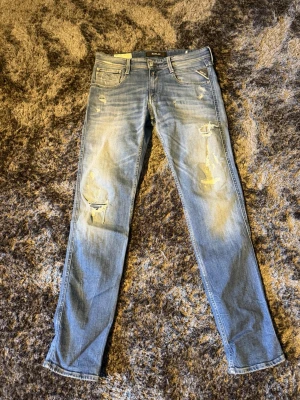 Replay jeans  - Säljer ett par ljusblå jeans från Replay med skinny fit och slitningar på både lår och knän. Jeansen har klassisk femficksmodell, dragkedjegylf och patch med logga bak. Perfekta för en avslappnad streetstil.