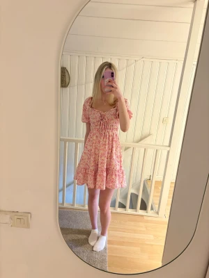 Rosa blommig klänning Gina Tricot - Supersöt kort klänning från Gina Tricot i rosa och vitt med blommigt mönster. Klänningen har puffärmar, rynkade detaljer framtill och en lätt utsvängd kjol. Perfekt för dig som gillar romantisk och feminin stil.