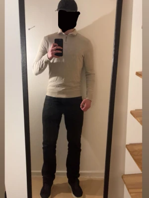 Beige stickad tröja med halv dragkedja - Snygg beige stickad tröja med halv dragkedja i kragen. Tröjan har lång ärm, ribbade muddar och en smal passform. Perfekt för lager-på-lager och enkel att matcha med jeans eller chinos.