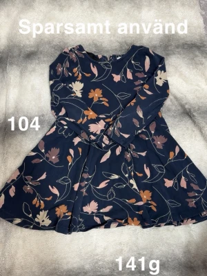 Mörkblå blommig klänning med långa ärmar - Mörkblå klänning med blommigt mönster. Klänningen har lång ärm och rund halsringning, samt en lätt utställd kjol. Perfekt för dig som gillar en söt och bekväm stil.🌸 Sparsamt använd. Storlek 104