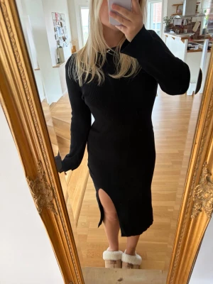 Svart ribbad långklänning med slits - Svart långärmad ribbad långklänning med en snygg slits framtill. Klänningen har en kroppsnära passform och rund halsringning. Perfekt för dig som gillar stilrena och enkla plagg med en twist.
