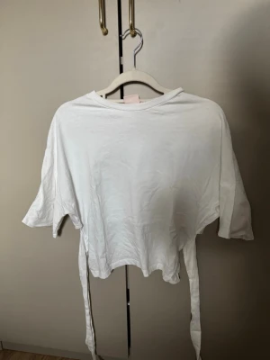 Vit croppad topp med knytband - Snygg vit croppad topp med knytband i sidorna och korta ärmar. Perfekt till höga jeans eller kjol. Enkel och stilren design med rund halsringning. 