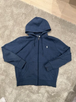 Mörkblå hoodie från Polo Ralph Lauren - Mörkblå hoodie med dragkedja från Polo Ralph Lauren. Klassisk design med huva, nypris 2200kr kvitto finns!