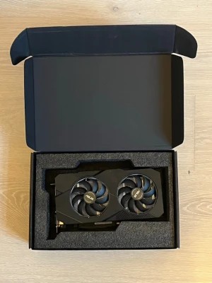 ASUS 1660 grafikkort med dubbla fläktar - Säljer ett svart ASUS grafikkort med två stora fläktar för effektiv kylning. Kortet har en modern design med mattsvart finish och är tillverkat i metall och plast. Perfekt för gaming eller krävande grafikapplikationer. Levereras i originalförpackning med skyddande skum.