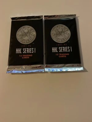 NHL Pro Set Platinum 1991-92 Series I - Två oöppnade paket NHL Pro Set Platinum 1991-92 Series I samlarkort, varje paket innehåller 12 trading cards. Svart och silverfärgad förpackning med tydlig logga och text. Perfekt för dig som gillar hockeykort och samlarprylar.