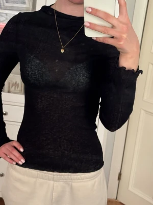 Svart långärmad topp från Gina Tricot - Säljer en svart långärmad topp från Gina Tricot. Toppen är tunn och transparent med lätt ribbad struktur och har en enkel, tight passform. 