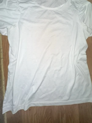 Vit t-shirt med puffärm från Vila - En enkel och fräsch vit t-shirt från Vila med puffade axlar som ger en trendig touch. T-shirten har rund halsringning och är tillverkad i mjuk bomull, perfekt för en clean och stilren look. Har använt 2 gånger.