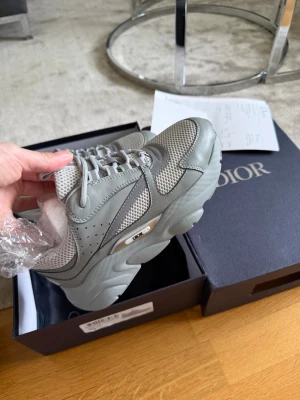 Gråa sneakers i mesh och läder - Snygga sneakers i ljusgrått och vitt med detaljer i både mesh och läder. Skorna har en chunky sula, klassisk snörning och coola paneler som ger en modern vibe. Perfekta för dig som gillar stilrena och trendiga sneakers.Storlek 36 men passar även 37