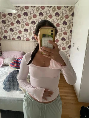 Ljusrosa långärmad topp - Söt ljusrosa långärmad topp med rundad halsringning och figurnära passform. Toppen är tillverkad i mjuk bomull och har långa ärmar med lätt utsvängda ärmslut. Perfekt att styla med jeans eller kjol för en trendig look.