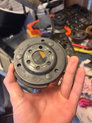 Polini koppling  - Rund metallskiva med flera hål och spår, troligen en del till maskin eller fordon. Skivan är grå och har en robust känsla med flera cirkulära och fyrkantiga öppningar. Perfekt för dig som gillar att meka eller behöver reservdelar till projekt.