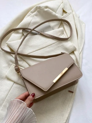 Beige axelväska med gulddetalj - Stilren beige axelväska med lång justerbar rem och elegant guldfärgad metallspänne på framsidan. Väskan har en rektangulär form och är tillverkad i slätt syntetmaterial. Perfekt för dig som gillar minimalistisk design och neutrala färger.