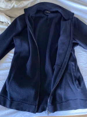 Marinblå ullrock med dragkedja - Snygg marinblå rock i ullmix från Massimo Dutti med hel dragkedja framtill och hög krage. Rocken har en rak passform och diskreta fickor på sidorna. Perfekt för kyliga dagar och ger en clean look. Storlek M