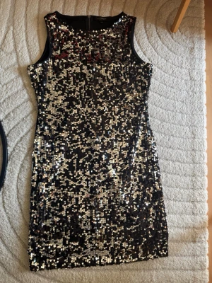 Svart paljettklänning KappAhl - Snygg svart kortklänning från KappAhl täckt med glittriga silverfärgade paljetter. Ärmlös modell med rund halsringning och dragkedja i ryggen. Perfekt för dig som vill sticka ut på festen!