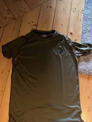 Olivgrön t-shirt från gorilla wear - Snygg olivgrön t-shirt från gorilla wear med diskret logga på bröstet. Tillverkad i mjuk polyester som andas, perfekt för träning eller chill. Klassisk passform med korta ärmar och rund halsringning.