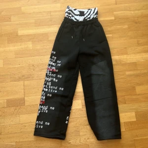 eyehategarments Svarta mjukisbyxor med texttryck - Unika svarta mjukisbyxor med vitt och rött texttryck längs ena benet och zebra-mönstrad midja. Vida ben och resår i midjan för skön passform. Perfekta för dig som vill sticka ut med en streetwear-look.