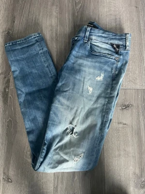 Blå slitna jeans från Replay - Säljer ett par blå jeans från Replay med skinny fit och slitningar på både lår och knän. Jeansen har klassisk femficksdesign, låg midja och är tillverkade i denim med tvättad effekt. Perfekta för en avslappnad och trendig look. Hör av för frågor o funderingar 