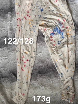 Blommiga byxor med mudd - Gula byxor med blommönster. Byxorna har resår i midjan och vid bensluten samt volangkant längst ner. Perfekt för dig som gillar en söt och avslappnad stil.🌸 Fläckar. Storlek 122/128