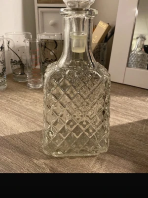 Karaff i mönstrat glas med lock - Säljer en stilren karaff i transparent glas med rutmönster och tillhörande glaslock. Perfekt för att servera drycker eller som snygg inredningsdetalj. Klassisk form och tidlös design som passar i de flesta hem.