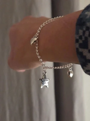 Silverfärgat armband med berlocker Rostfritt Stål  - Snyggt silverfärgat armband i rostfritt stål med kedja och tre berlocker: två hjärtan och en stjärna med texten 'I love you'. Perfekt accessoar för att ge din outfit en personlig touch. Armbandet har en enkel och stilren design som passar till många olika stilar. Handgjort.